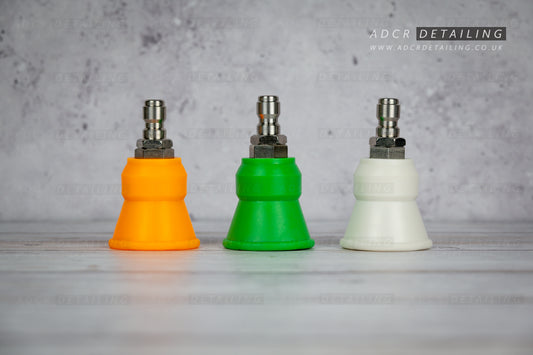 Three coloured car detailing 1/4in quick release premium rubber protector pressure washer nozzles on a grey surface with a concrete wall background.