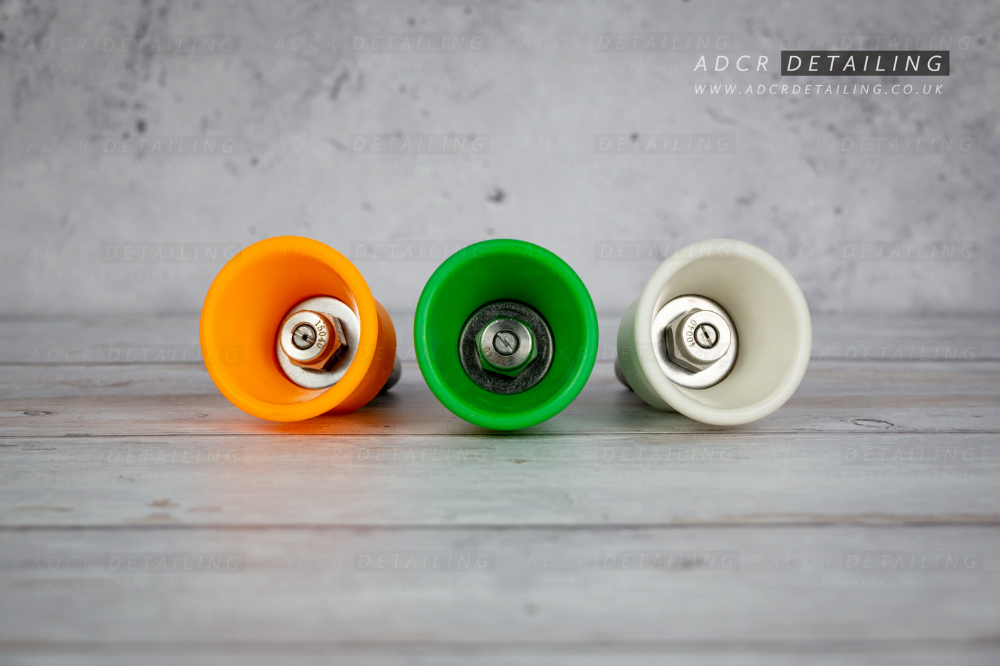Three car detailing pressure washer premium quick release nozzles in orange, green, and white on a wooden surface with a grey background.