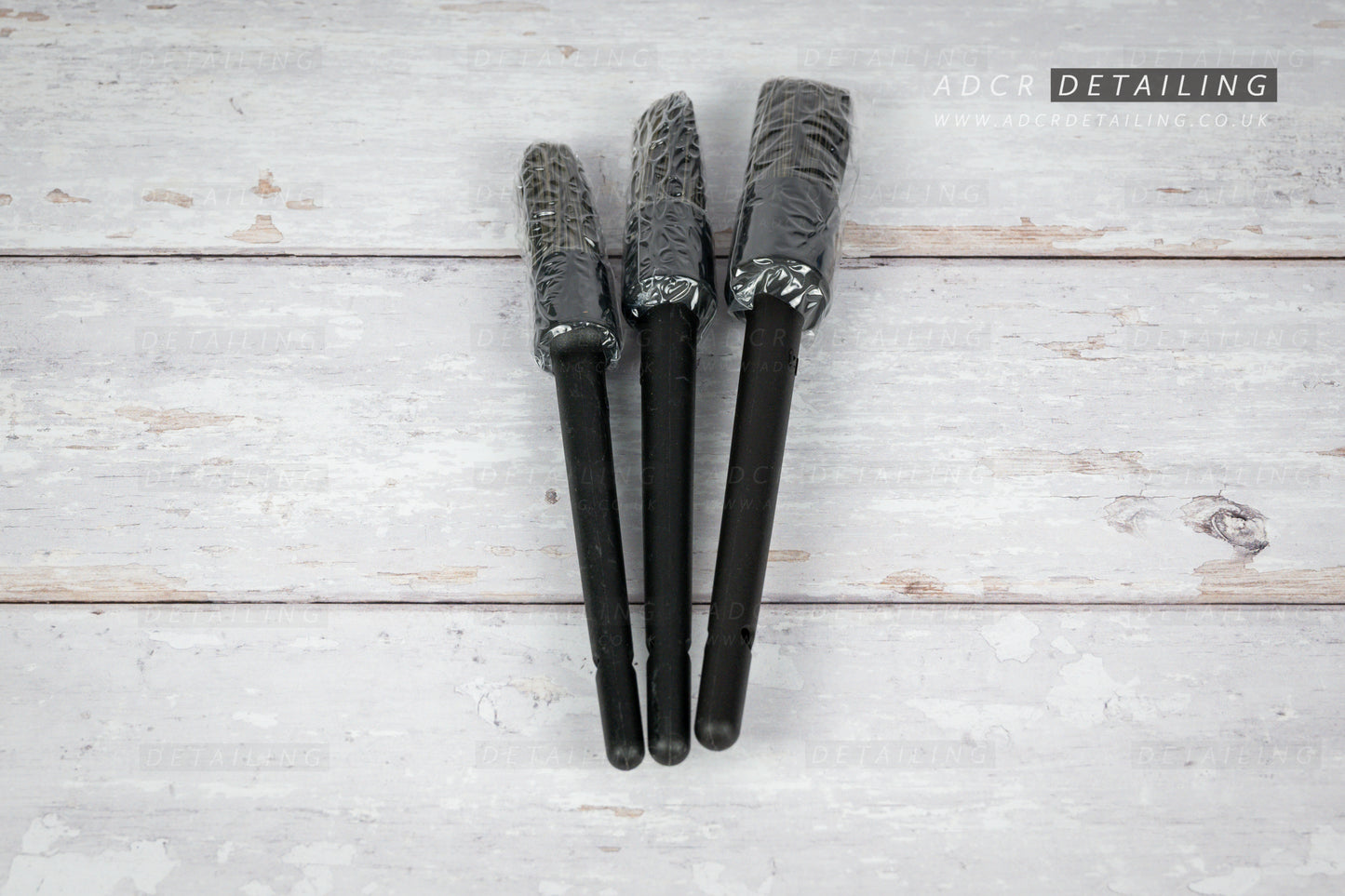 Three black car detailing brushes on a light wooden surface with 'ADCR Detailing' logo.