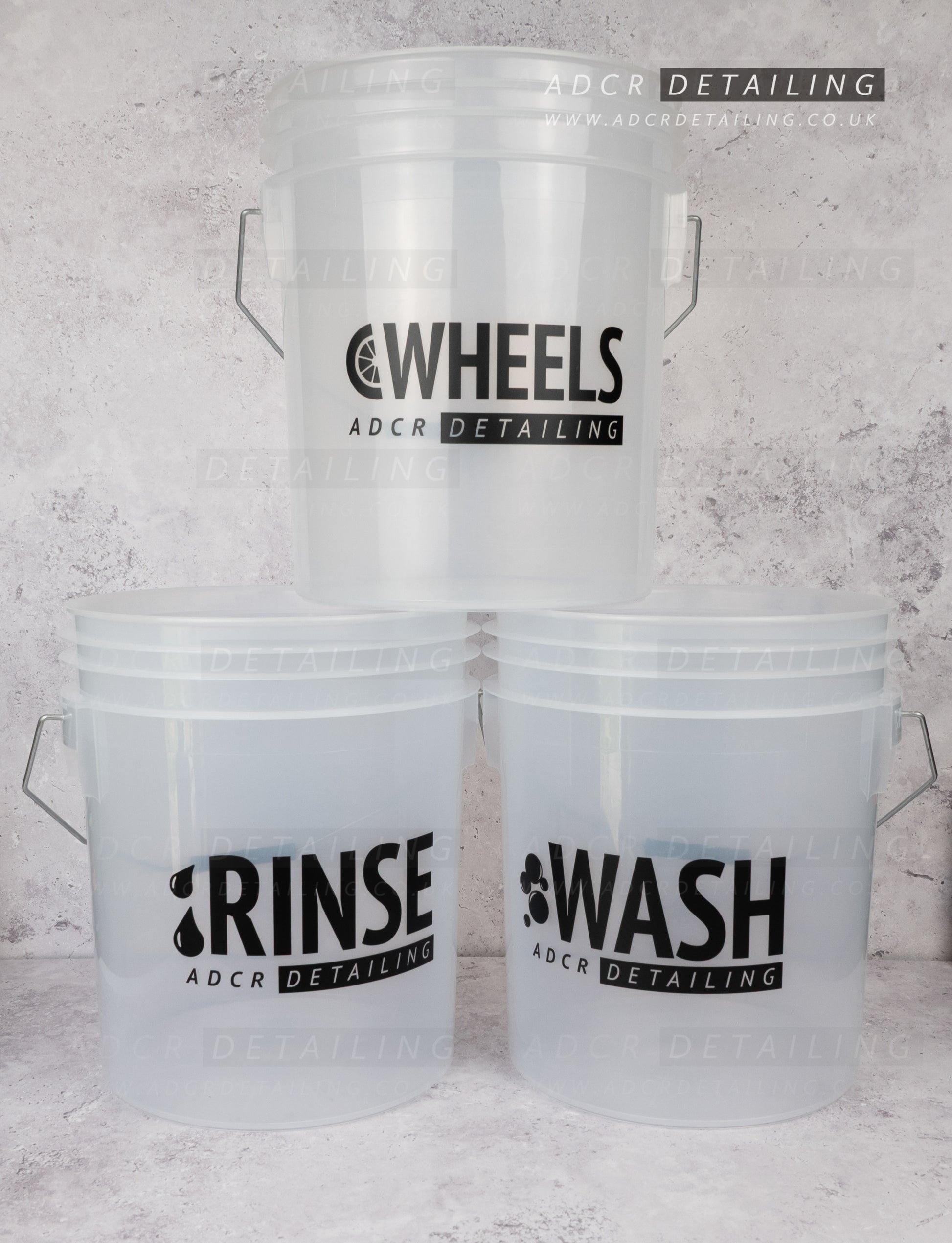 Three clear detailing and valeting buckets with 'WASH', 'RINSE', and 'WHEELS' labels on a concrete background.