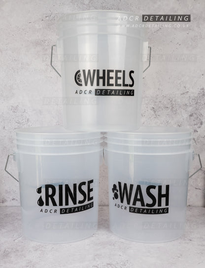 Three clear detailing and valeting buckets with 'WASH', 'RINSE', and 'WHEELS' labels on a concrete background.