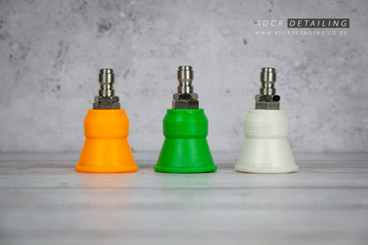 Three coloured car detailing 1/4in quick release premium rubber protector pressure washer nozzles on a grey surface with a concrete wall background.