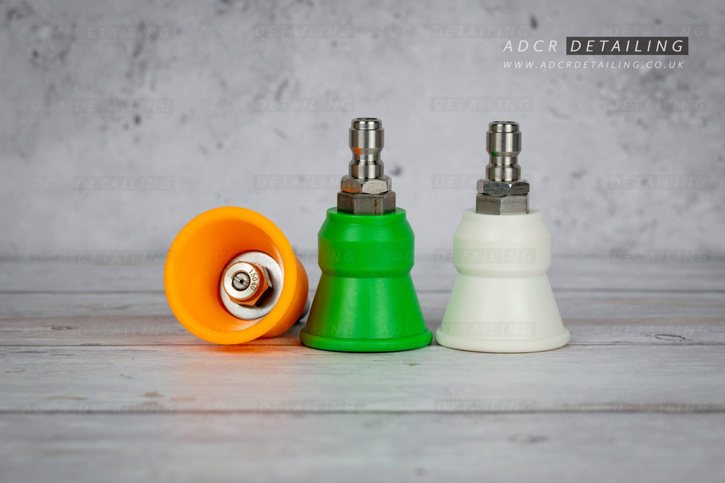 Three pressure washer detailing rubber spray nozzles in orange, green, and white on a wooden surface with a gray background.