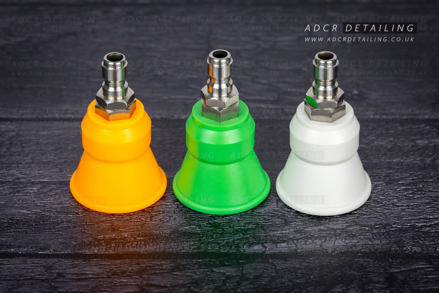 Three car detailing spray nozzles in orange, green, and white on a dark wooden surface with 'ADCR Detailing' branding.