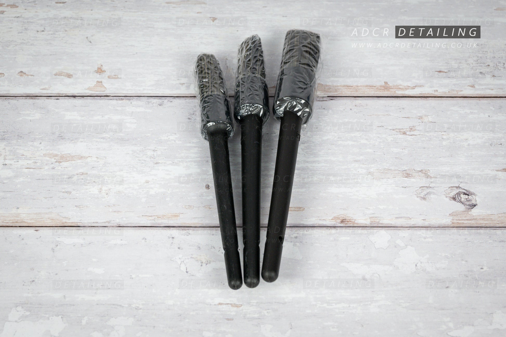 Three black car detailing brushes on a light wooden surface with 'ADCR Detailing' logo.
