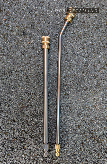 Two metal pressure washer extension bars with quick release connectors, one straight and one angled, lying on a textured surface.